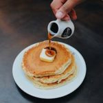 Delicious stack of pancakes topped with butter and maple syrup being poured.
