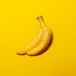 A bunch of ripe yellow bananas against a vivid yellow backdrop, offering tropical freshness.