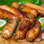 Juicy grilled sausages on a wooden board with lemon slices and herbs.