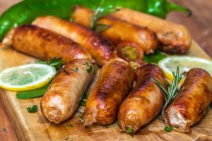 Juicy grilled sausages on a wooden board with lemon slices and herbs.